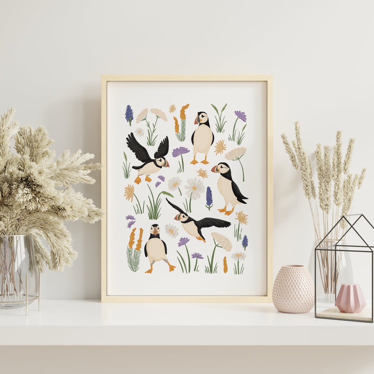 Puffin coastal wall art in a light wood frame styled on a neutral shelf with pottery and soft natural decor.