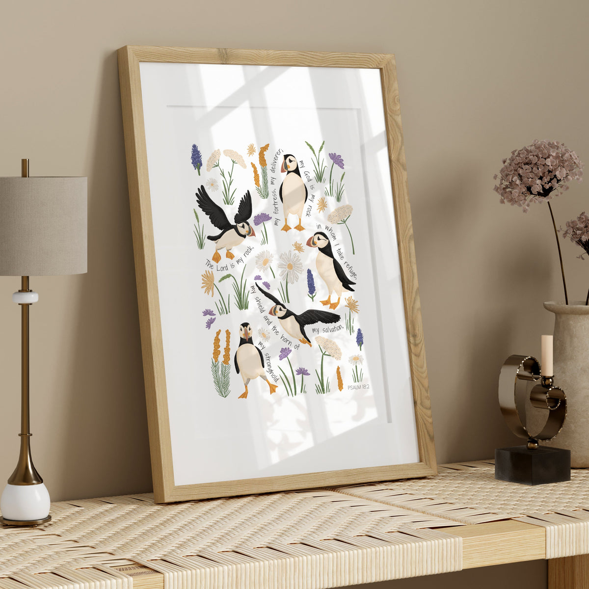 Puffin and sea holly scripture art print in a light wood frame styled above a console table with simple natural accessories.