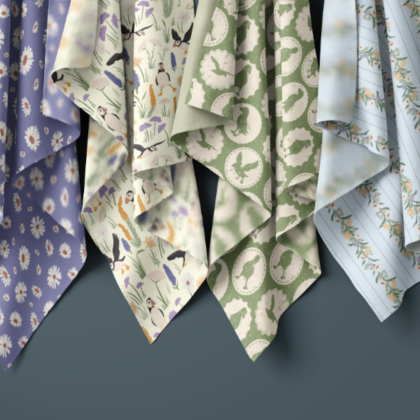 Five folded patterned fabric napkins or small scarves hanging against a dark gray background. The fabrics show different prints: lavender with white floral motifs, cream with birds and foliage, sage green with circular motifs, and white with delicate botanical lines.