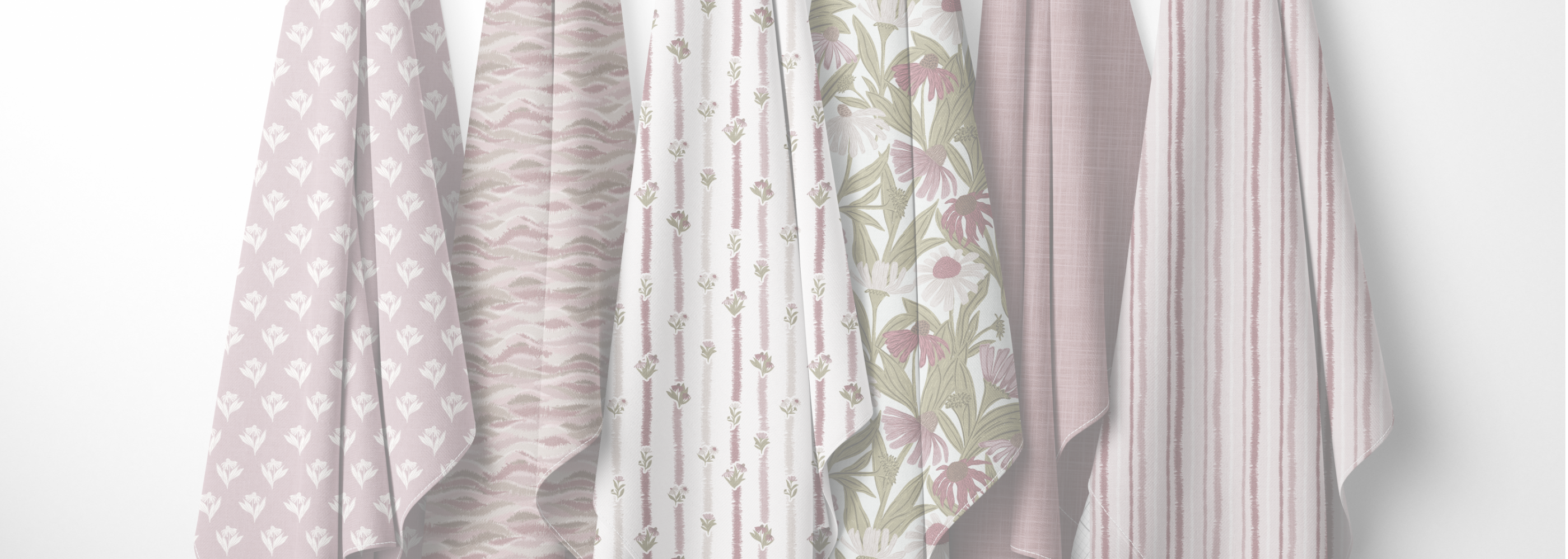 Six fabric panels in soft blush, beige, white, and floral green patterns hanging side-by-side against a plain white wall.