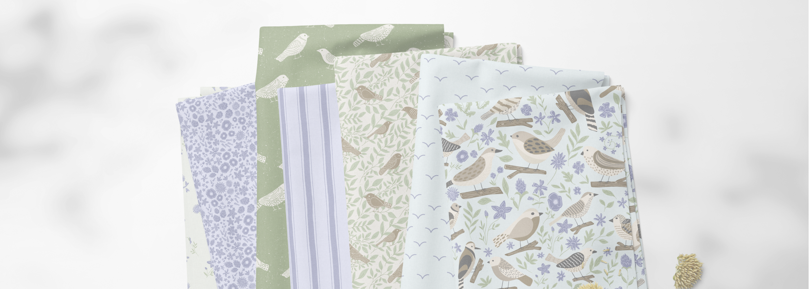 A stack of folded fabric pieces with various patterns including stripes, florals, and birds, displayed on a light gray marble-textured background.