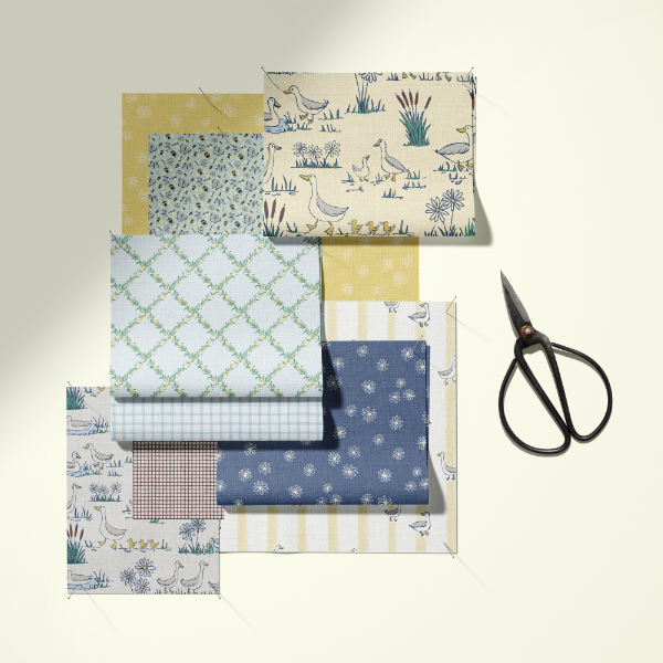 A set of folded fabric swatches in various patterns (geometric, floral, stripes, nature prints) arranged on a light cream background next to a pair of black-handled scissors.