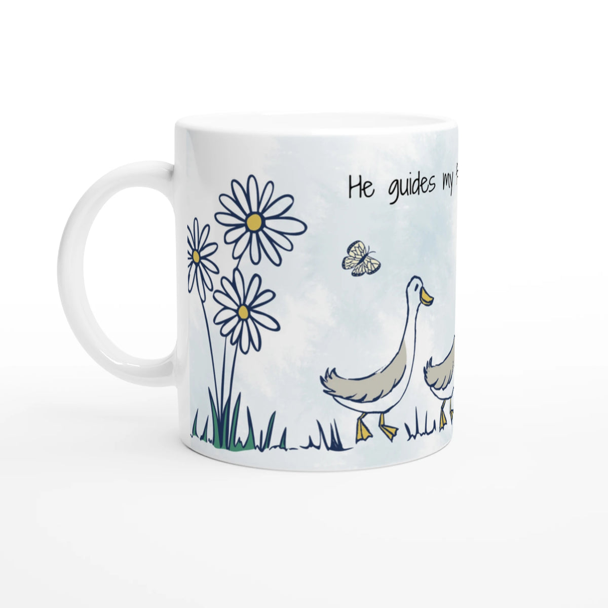 A white ceramic mug featuring a printed illustration of two white and gray geese walking in a field, accompanied by daisies, a butterfly, and the text 'He guides my.