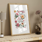 Hand-illustrated floral art print in a light wood frame styled on a neutral shelf with simple natural accessories.