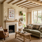 Christian floral wall art displayed above a fireplace in a bright country living room with exposed wooden beams.