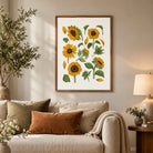 Hand-drawn sunflower wall art in a light wood frame above a cosy neutral sofa with warm earthy cushions and soft cottagecore styling.